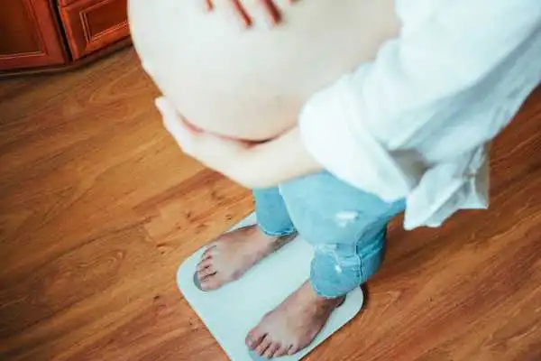 Image of woman weighing herself and experiencing weight gain through pregnancy Stockport